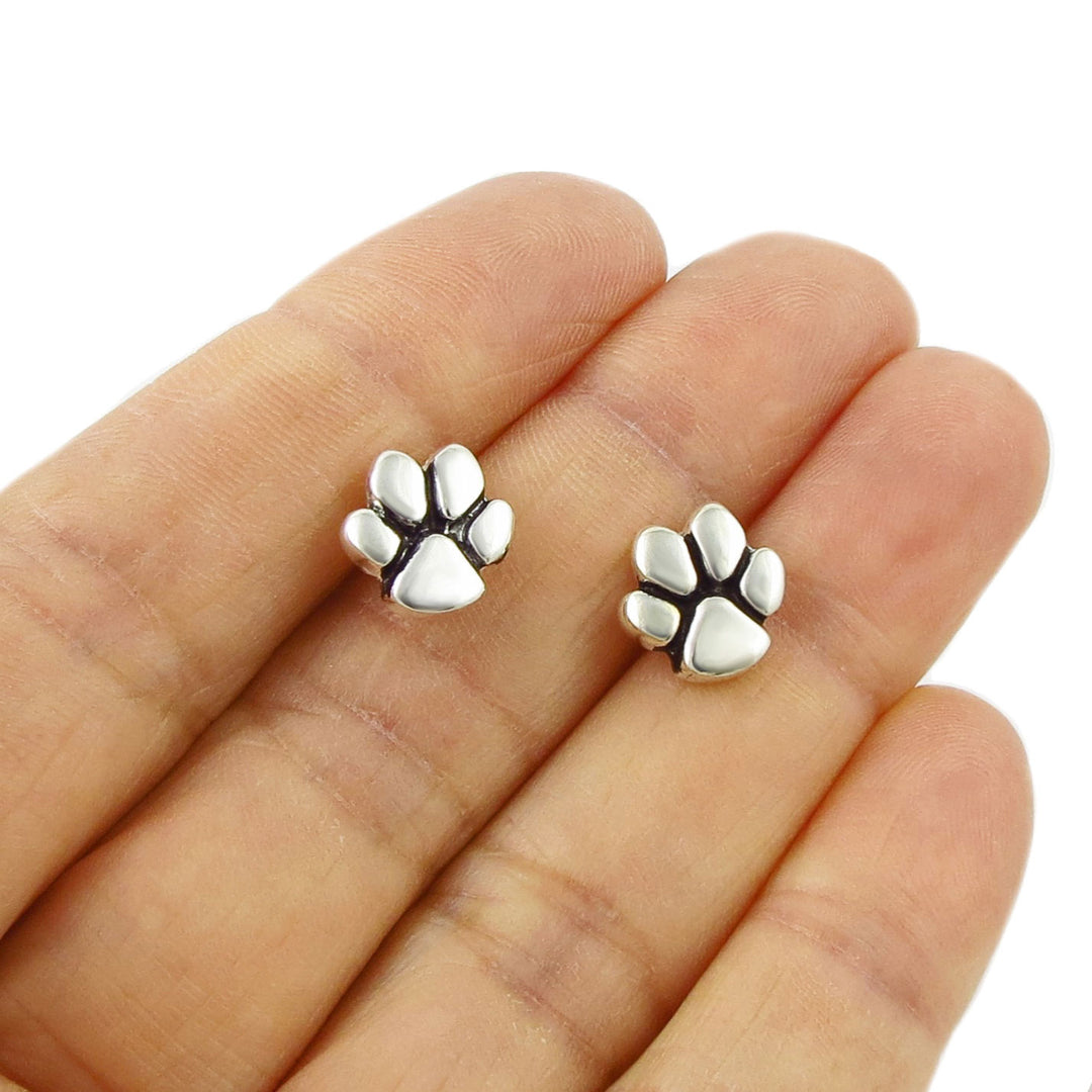 Sterling 925 Silver dog cat animal paw print stud earrings held between fingers on a white background