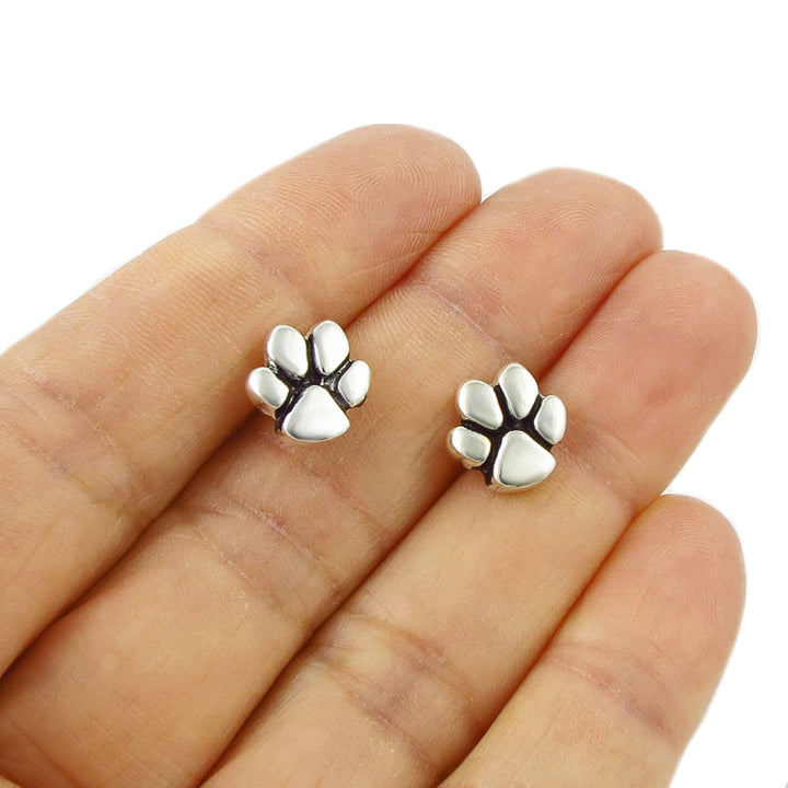 Sterling 925 Silver dog cat animal paw print stud earrings held between fingers on a white background