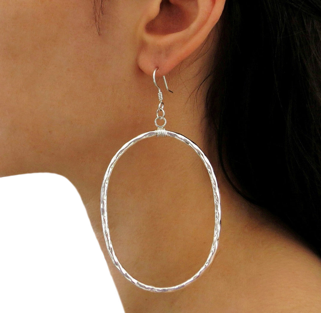 A large handmade 925 sterling silver hoop earring with a hammered finish worn by a woman with dark hair