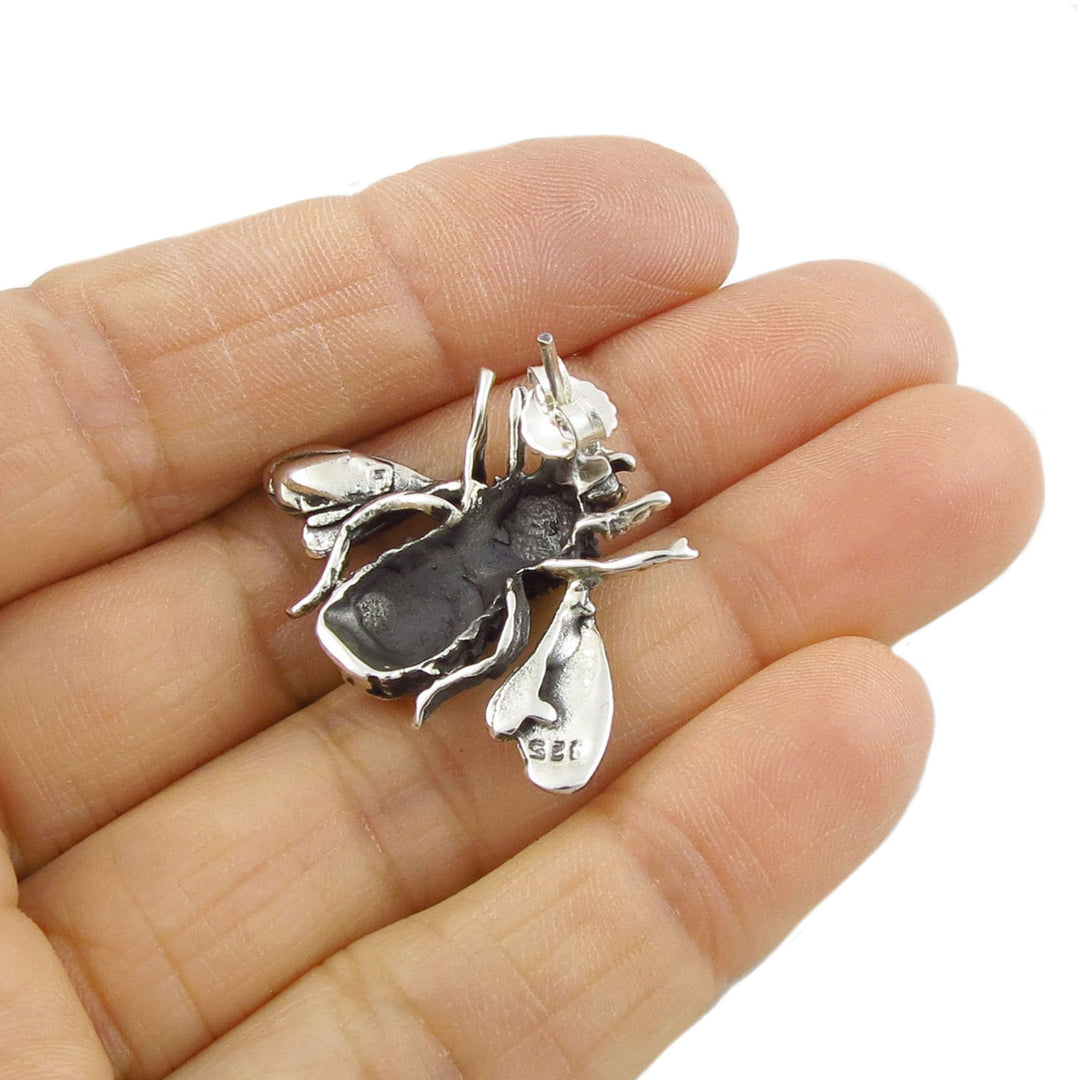 A llarge sterling silver bee shaped earring held upsaide down in a hand to show the 925 hallmark