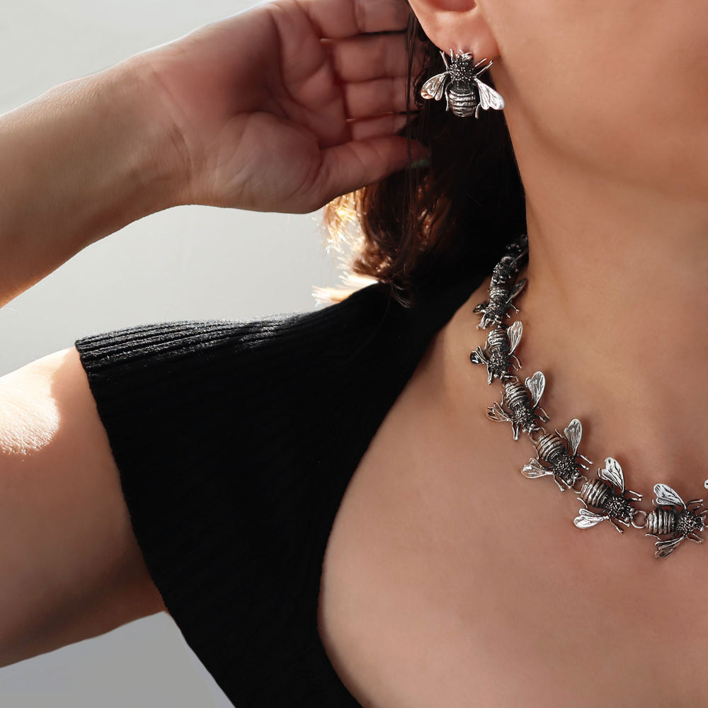 Large sterling 925 silver handmade bee insect stud earrings and matching necklace worn by a woman in a black top