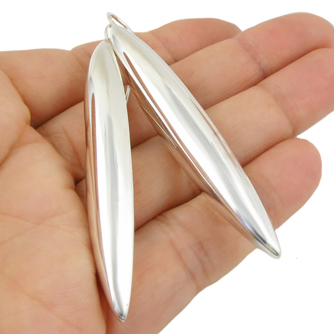 Long sterling silver drop earrings held in a hand against a white background