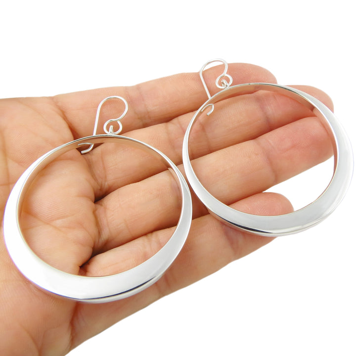 Silver hoop earrings held in a hand against a white background