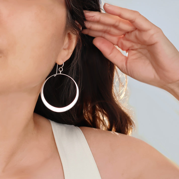 Close-up of a person wearing large silver hoop earrings with a neutral background