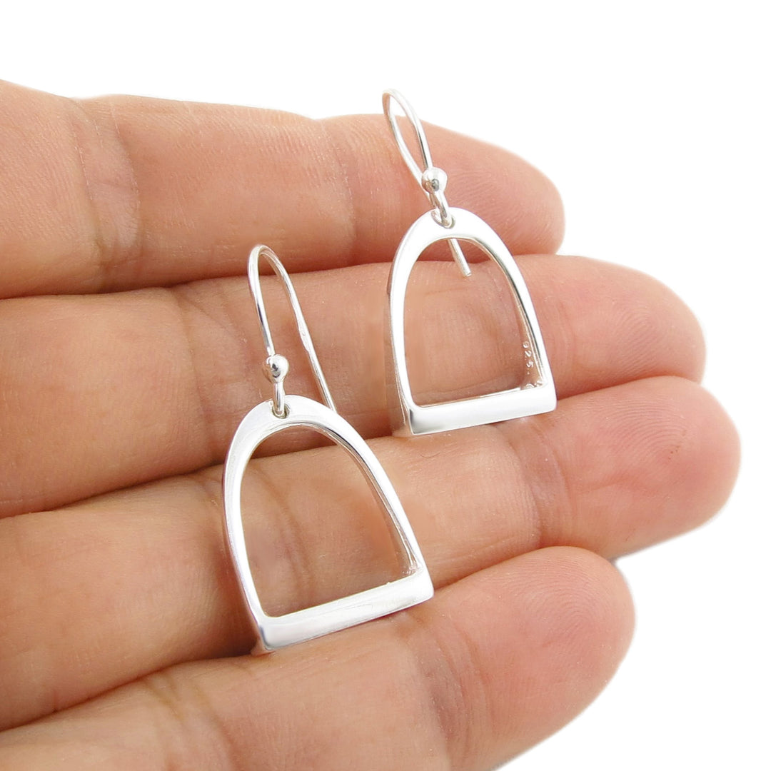 UK 925 sterling Silver dangling horse stirrup earrings held between fingers on a white background