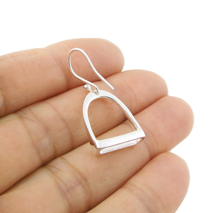 UK 925 terling Silver earring in the shape of a horse stirrup held between fingers on a white background