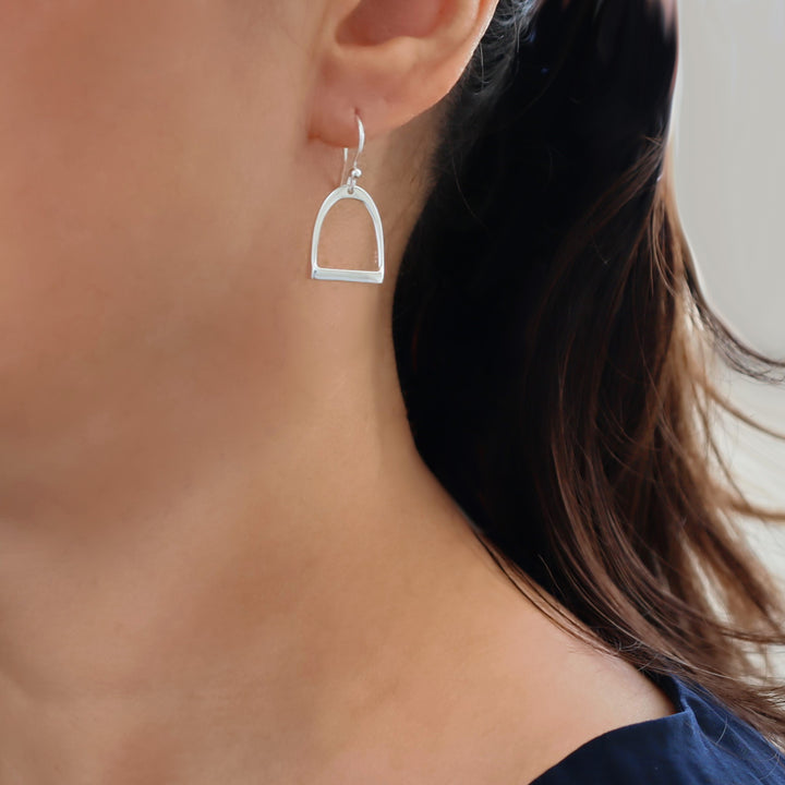 A large 925 sterling Silver earring resembling an equestrian horse stirrup worn by a woman with dark hair.