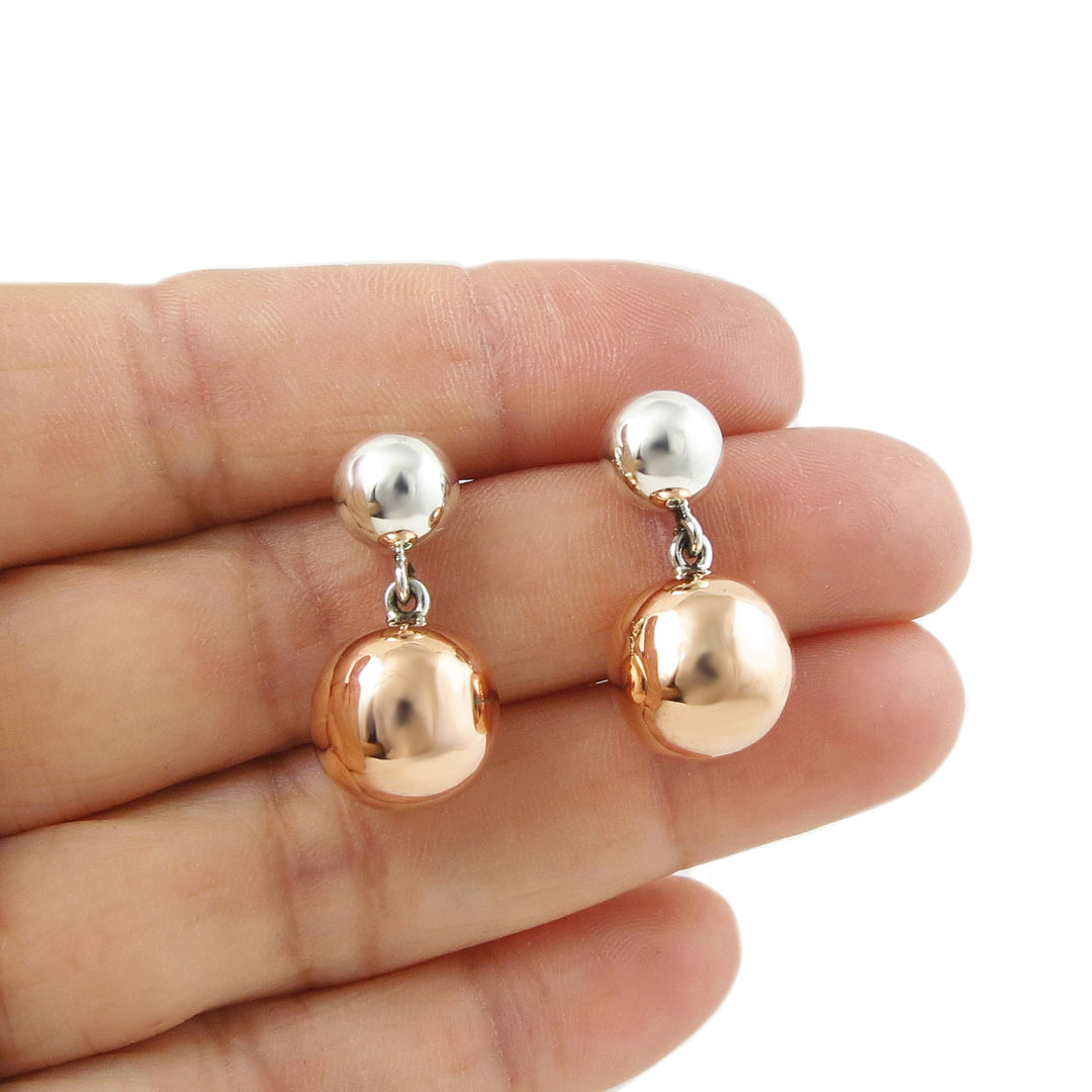 Mixed metal 925 silver and copper beaded ball earrings held in a person's hand on a white background