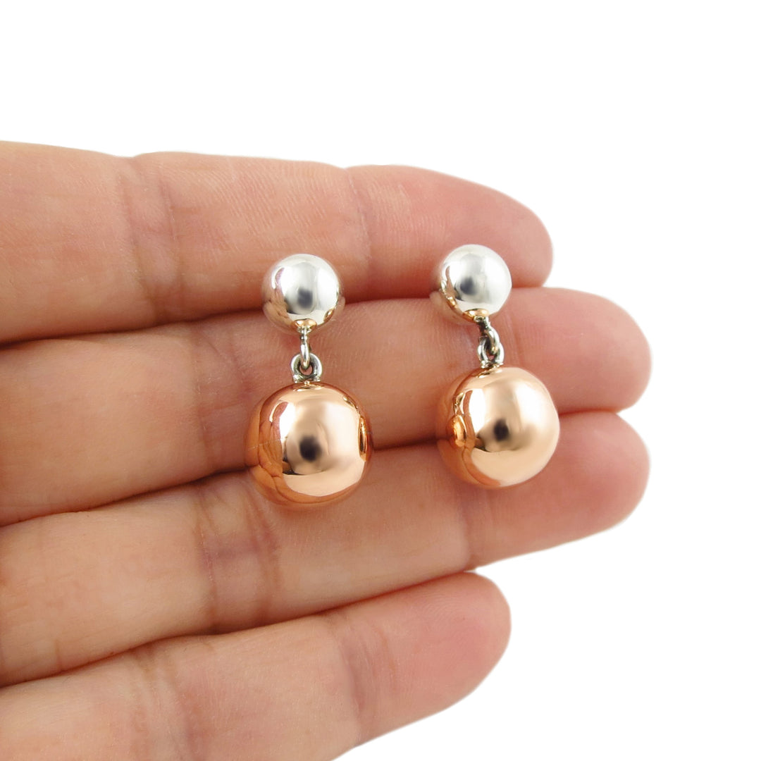Pair of copper and 925 silver mixed metal ball bead earrings held between fingers on a white background