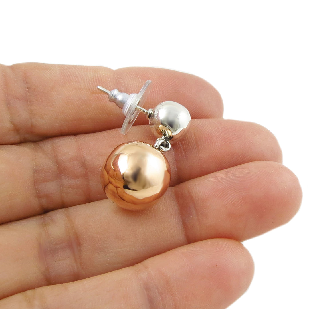 Two tone 925 silver and copper spherical ball earring held between fingers on a white background