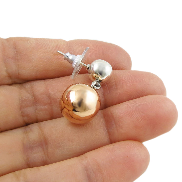 Two tone 925 silver and copper spherical ball earring held between fingers on a white background