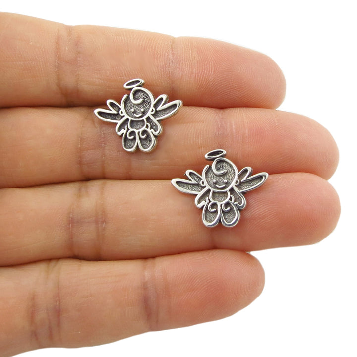 Two 925 silver angel stud earrings held between a woman's fingers on a white background