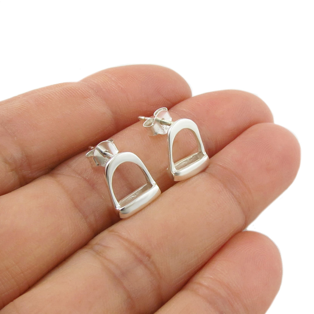 UK 925 sterling Silver equestrian stirrup earrings held between fingers on a white background
