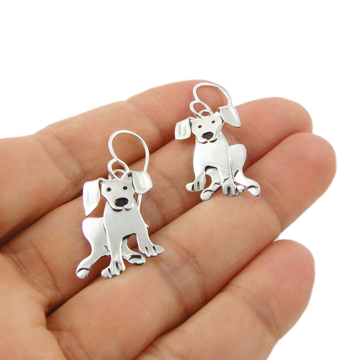 A pair of medium 925 silver labrador dog earrings displayed on a person's palm against a white background.