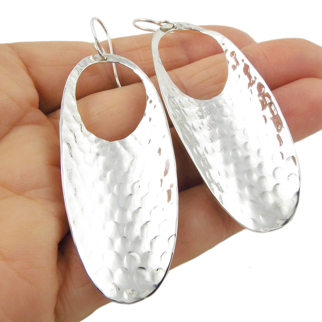 Silver hoop earrings with a hammered finish held in a hand against a white background