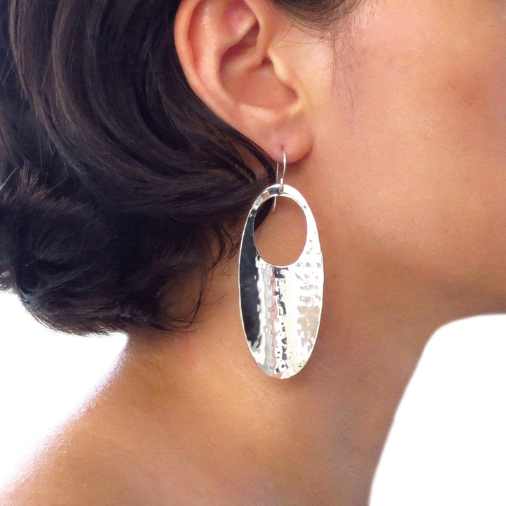 Silver drop earring with a hammered finish worn by a woman with a blurred background