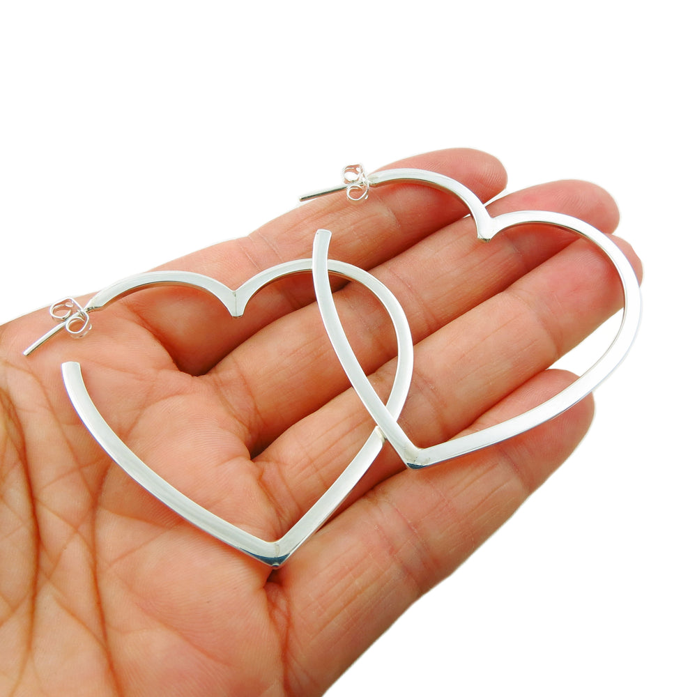 A pair of large love heart hoop earrings in 925 sterling silver held in a person's hand