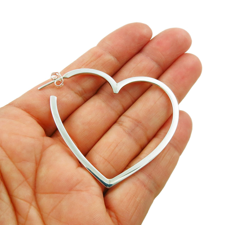 A single large heart shaped hoop earring held in a person's hand on a white background