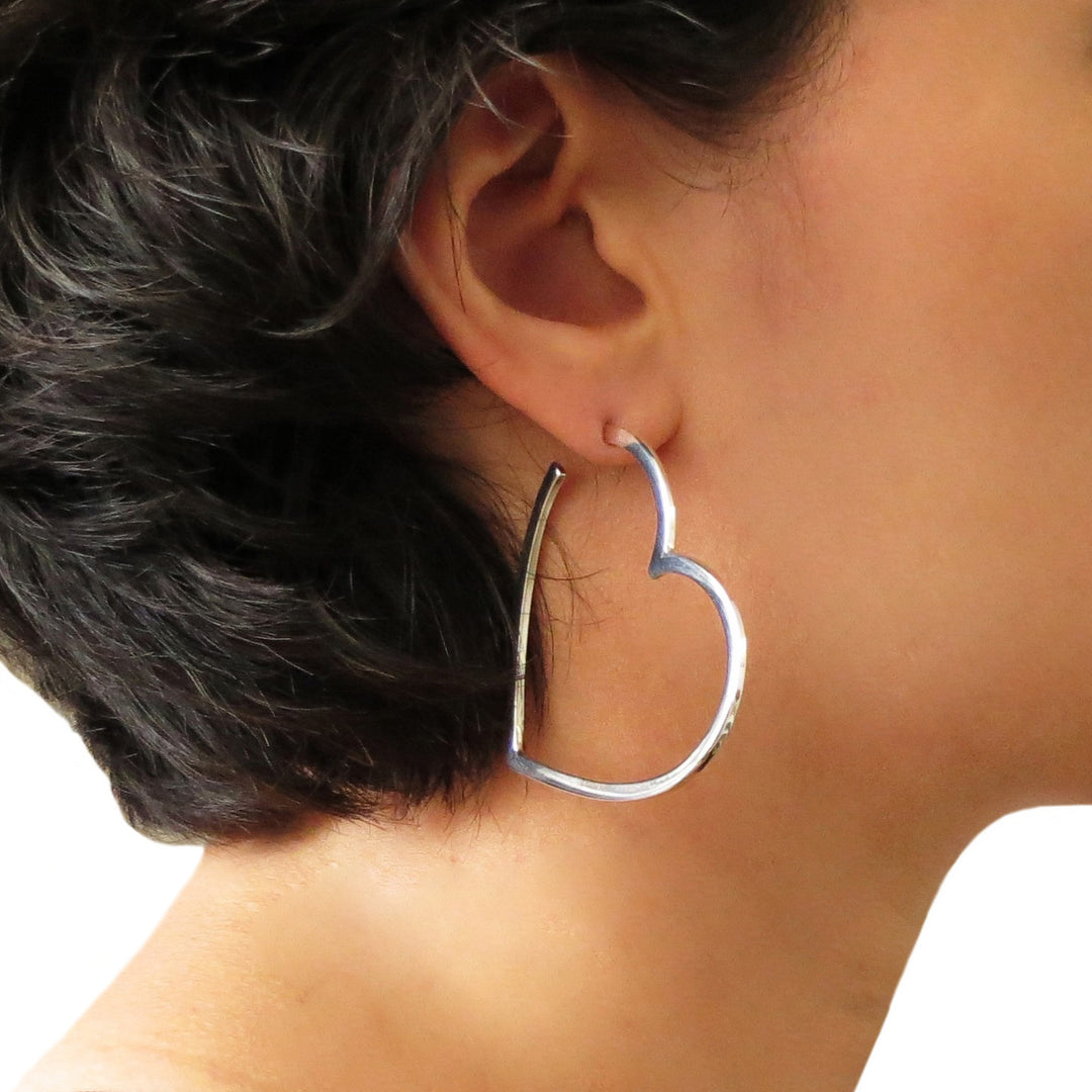 A woman with dark hair wearing a large hoop earring in the shape of a love heart