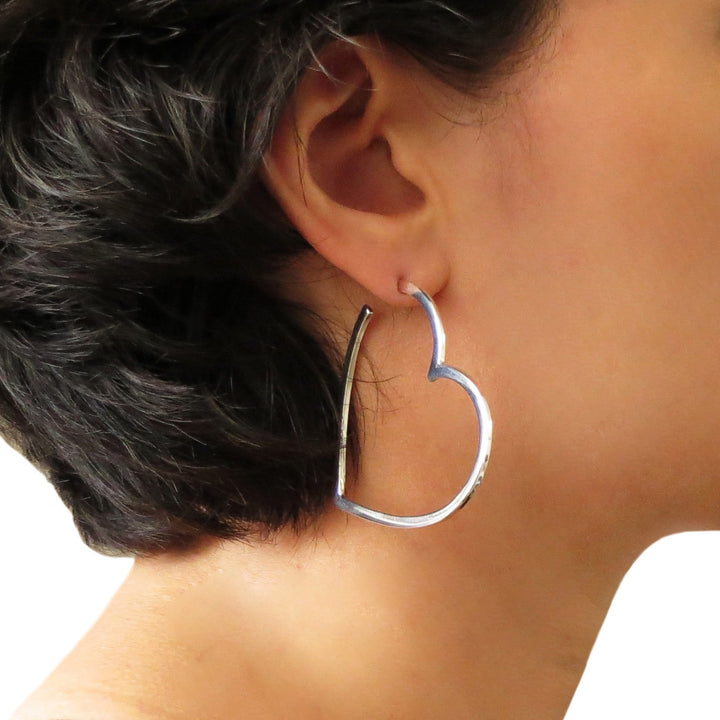 A woman with dark hair wearing a large hoop earring in the shape of a love heart