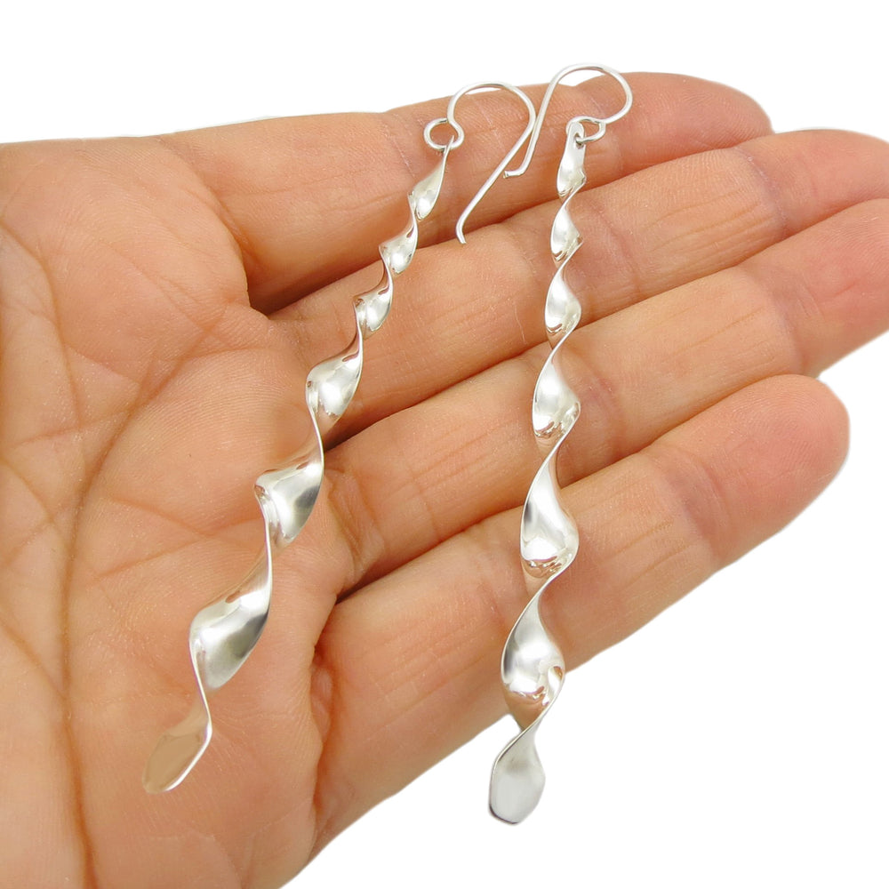 A pair of long twisted drop 925 sterling silver earrings held in a person's hand on a whuite background