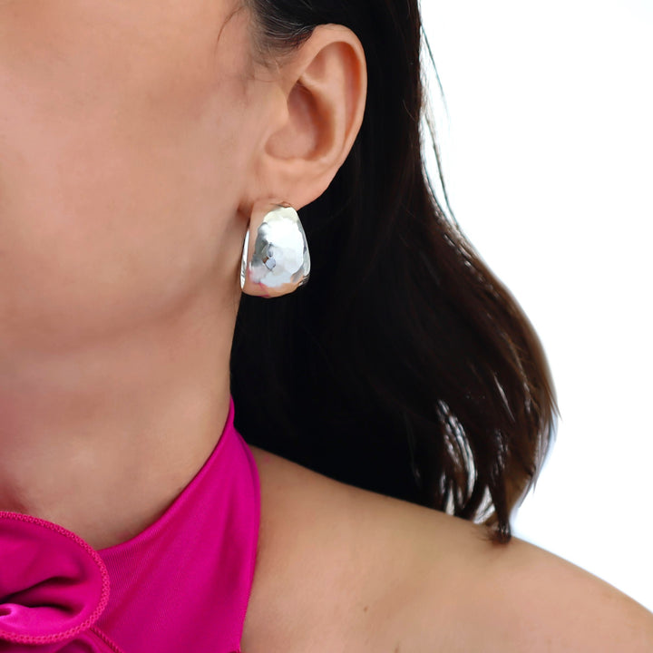 Close-up of a person wearing hammered silver hoop earrings with a blurred background