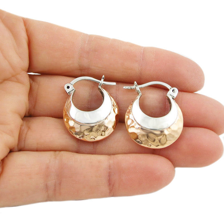 A pair of two tone creole hoop earrings made of copper and silver, displayed in a person's hand.