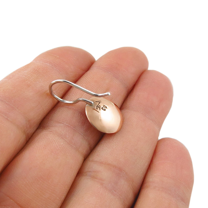Reverse of a single mixed metal copper and 925 silver round disc earring held on a person's fingers against a white background.