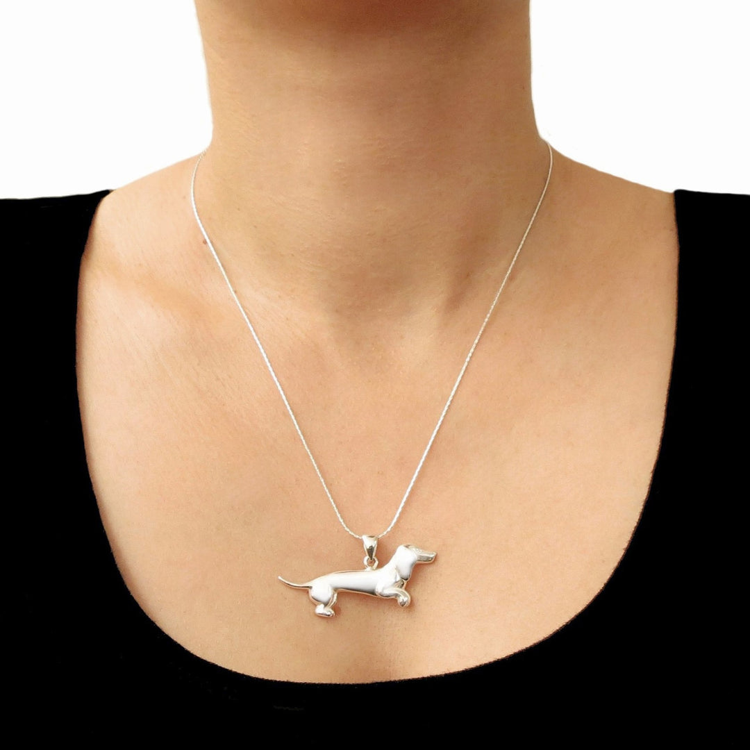 A 935 sterling silver dachshund pendant necklace worn on a woman's neck, shown against a black top and white background.