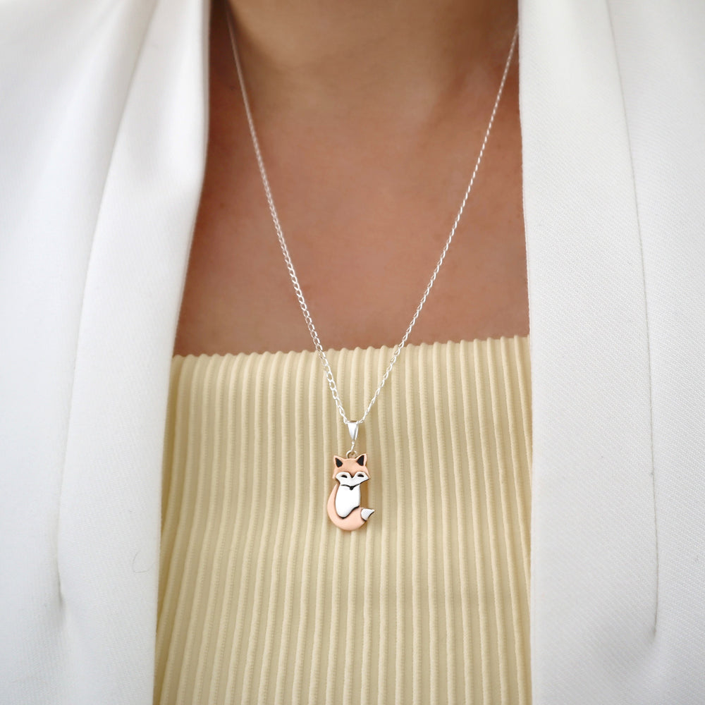 A person in a yellow top and white jacket wearing a unique two tone copper and 925 silver fox animal pendant and chain necklace