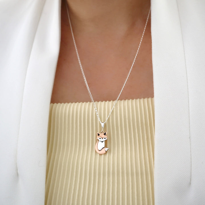 A person in a yellow top and white jacket wearing a unique two tone copper and 925 silver fox animal pendant and chain necklace