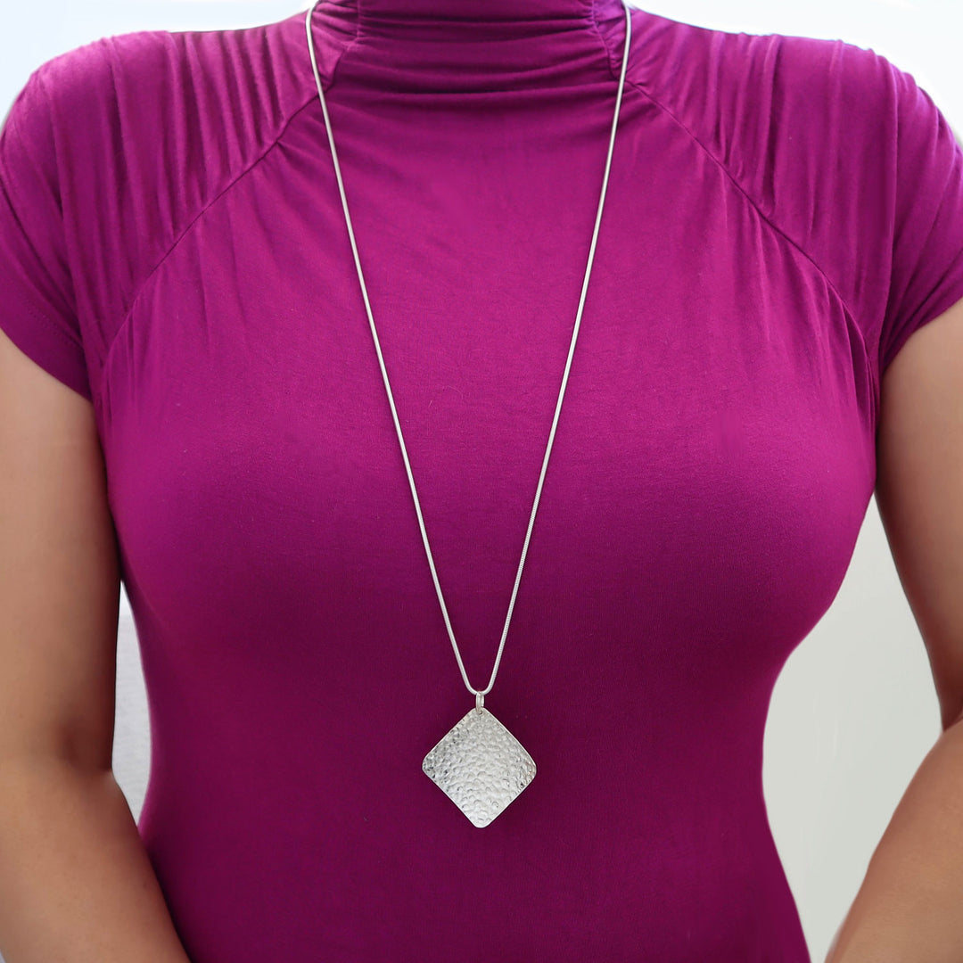 Woman wearing an extra long sterling 925 silver necklace with a hammered square shaped statememnt pendant on a purple top