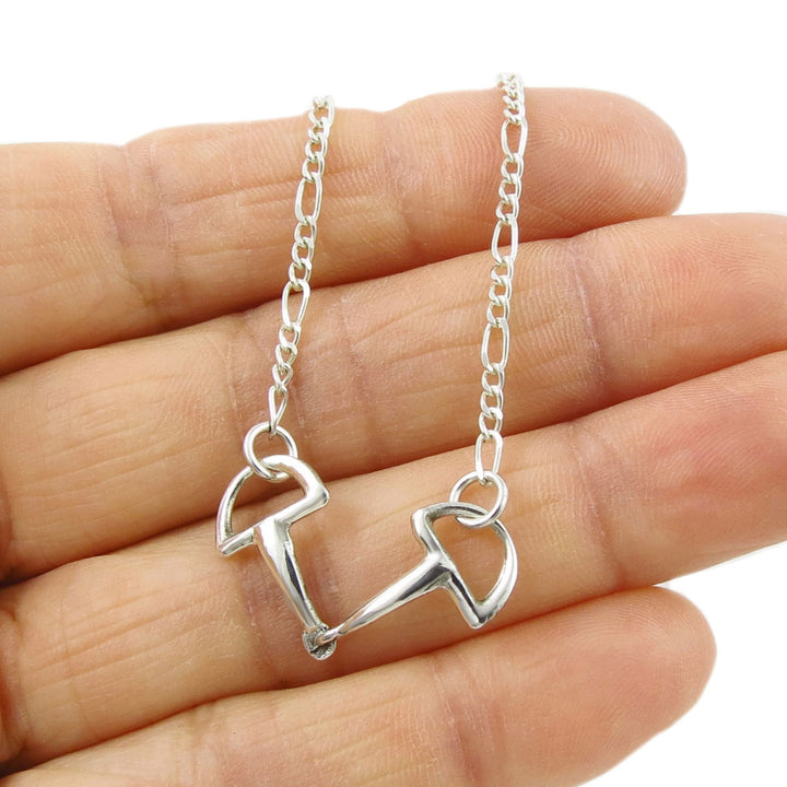A unique equestrian hore snafflebit pendant and igaro chain necklace held in a person's hand. 