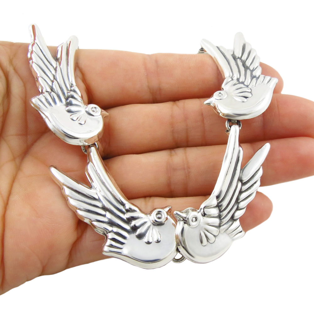 A large statement Mexican 925 sterling silver lovebird dove necklace held in a woman's hand against a plain white background.
