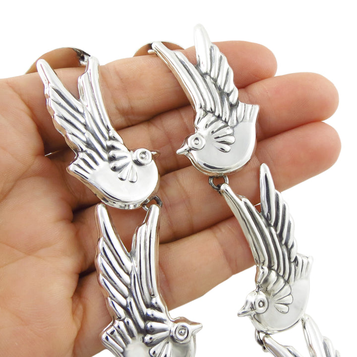 A hand holding a large 925 Mexican silver bird necklace, showing several polished silver love bird links with wings spread, set against a plain white background.