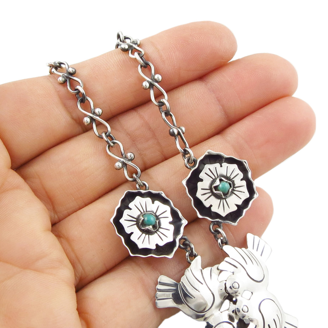 A large Mexican 925 sterling silver necklace with large lovebird and flower links decorated with natural turquoise gemstones, held in a woman's hand.