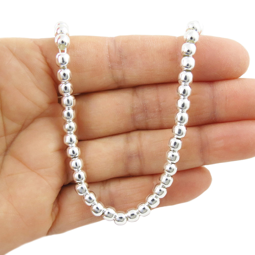 Silver beaded necklace held in a hand against a white background