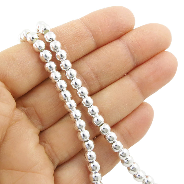 Silver beaded necklace held between fingers on a white background