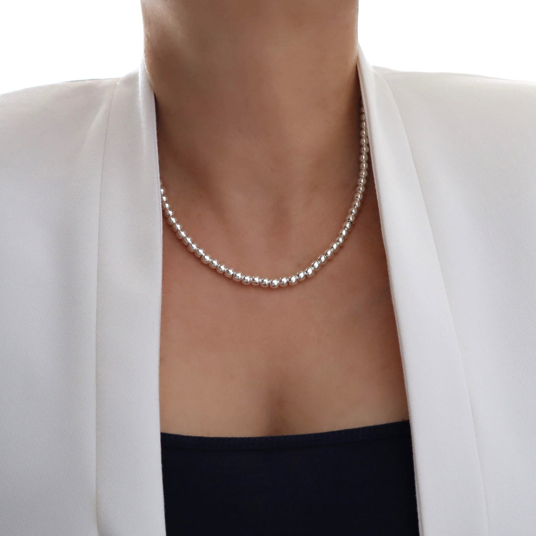 Silver ball bead necklace worn by a person with a white blazer and black top on a white background