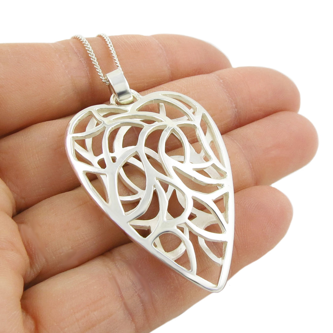 Silver heart-shaped pendant necklace held in a hand against a white background