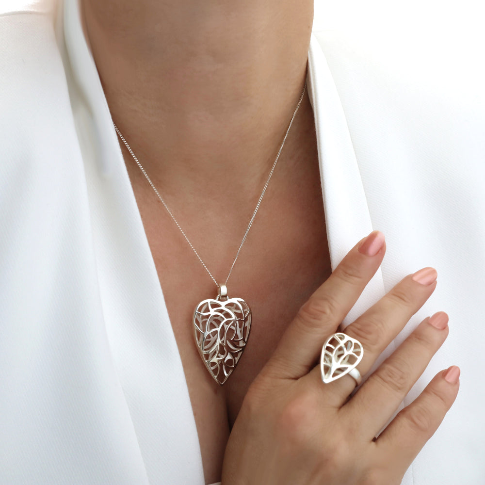 Silver heart-shaped pendant necklace and ring being worn by a person with a white jacket.
