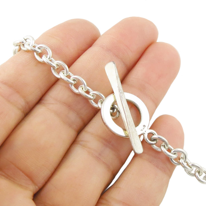 A sterling silver toggle clasp chain necklace being held in a hand against a plain white background.