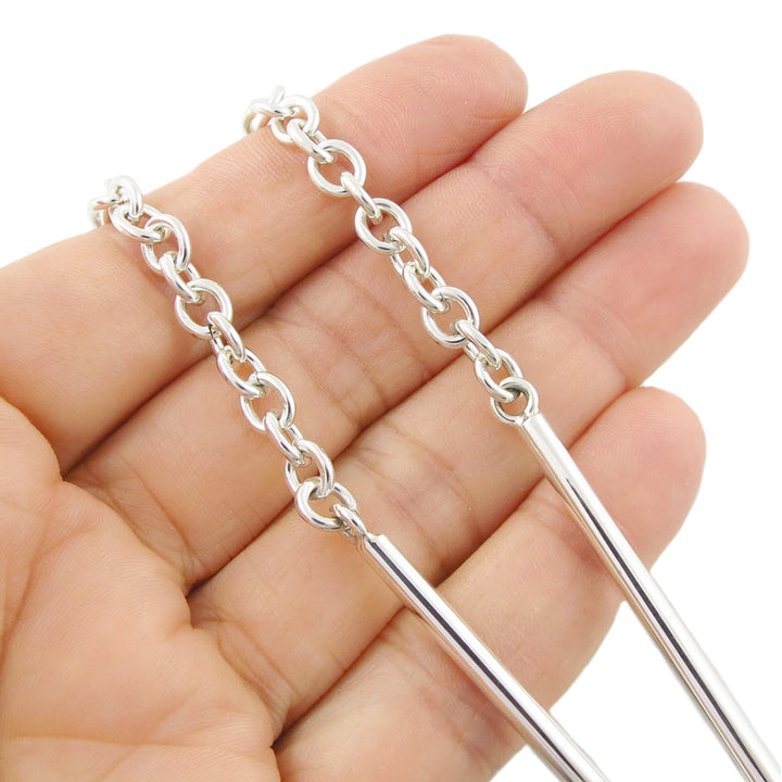 A close-up of a hand holding a modern sterling 925 silver chain necklace against a plain white background.