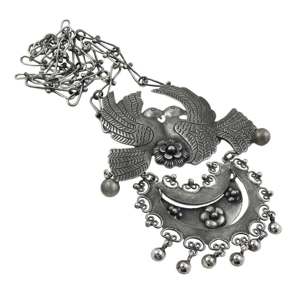 A large statement Mexican 925 sterling silver pendant necklace featuring stylised love birds with spread wings, a crescent moon, floral details, and dangling beads, shown on a plain white background.