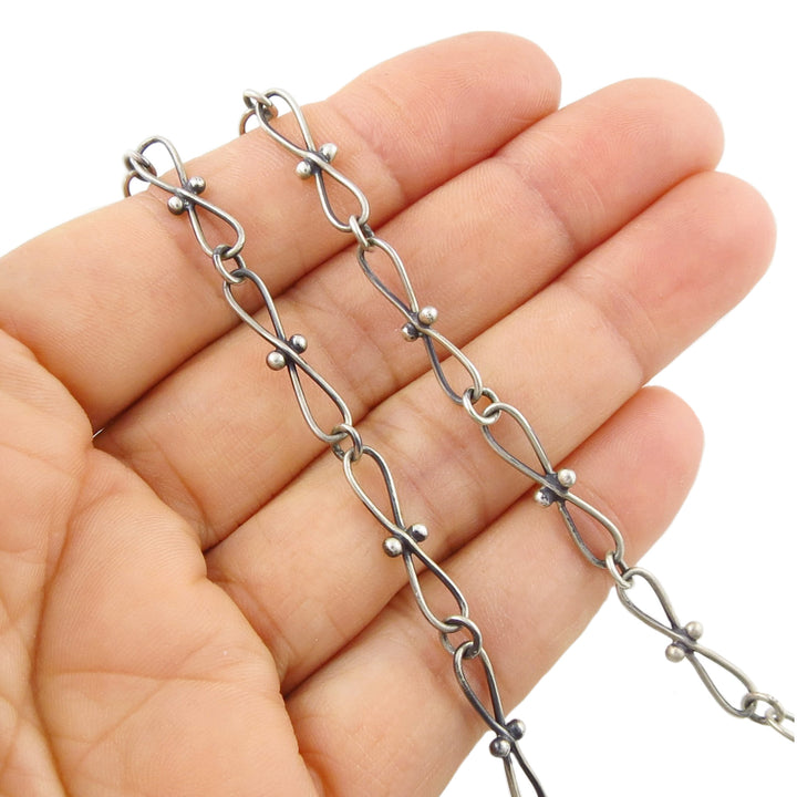 A close-up of a hand holding a 925 sterling silver fancy link chain necklace with elongated oval links and small bead accents, against a plain white background.