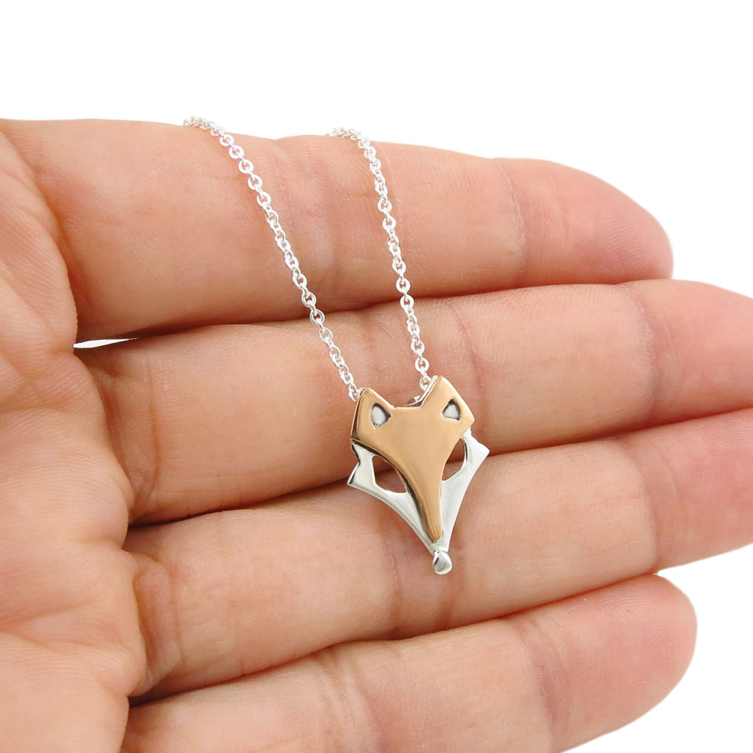 Two tone copper and 925 sterling silver fox-shaped pendant on a circle link chain held in a hand against a white background