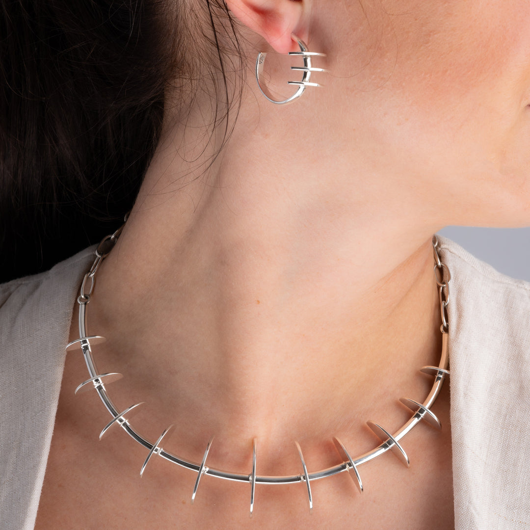 A close-up lifestyle shot of a model wearing a Mexican 925 silver spiked collar necklace and a matching silver hoop earring.