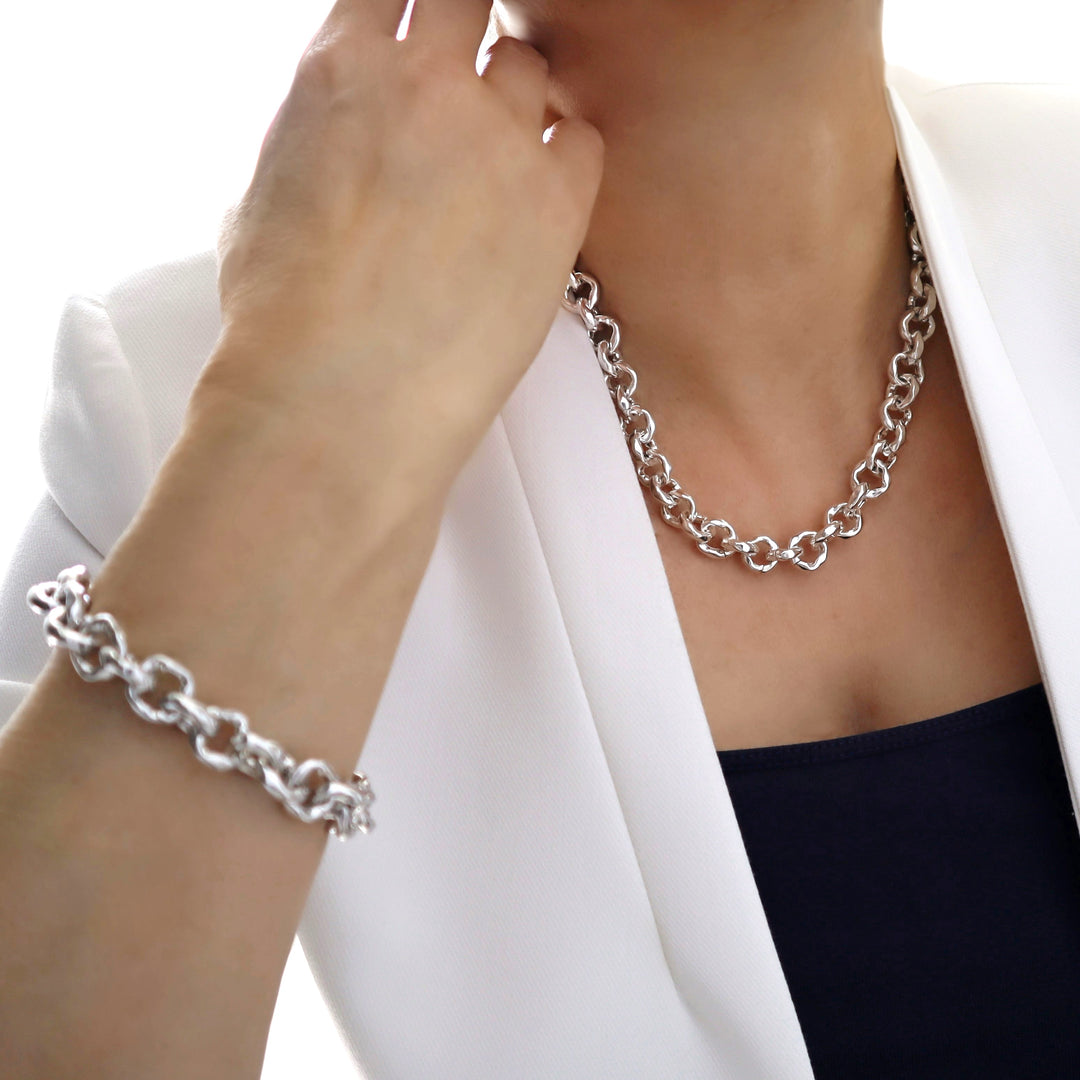 Person wearing a chunky silver chain necklace and bracelet against a white background