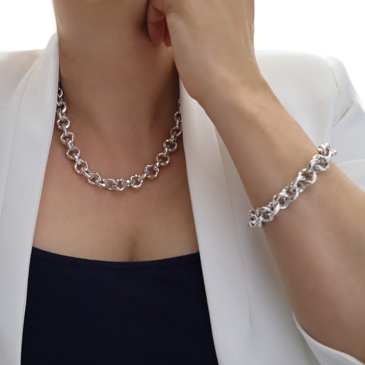 Person wearing a chunky silver chain necklace and bracelet on a white background