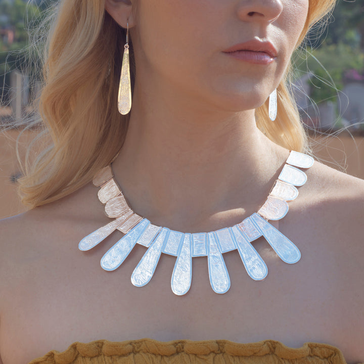 A close-up lifestyle shot of a model wearing a chunky silver statement necklace with teardrop-shaped silver discs and matching teardrop dangle earrings.